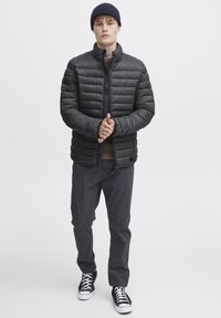Sort puffjakke med vandret sømme, stående krave og lynlås. Bæres med mørke bukser og sorte sneakers med hvide såler.