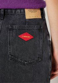 Svarta jeans i denim med en texturerad yta, med en röd diamantformad etikett som säger "LA MAISON AMY" på bakfickan.