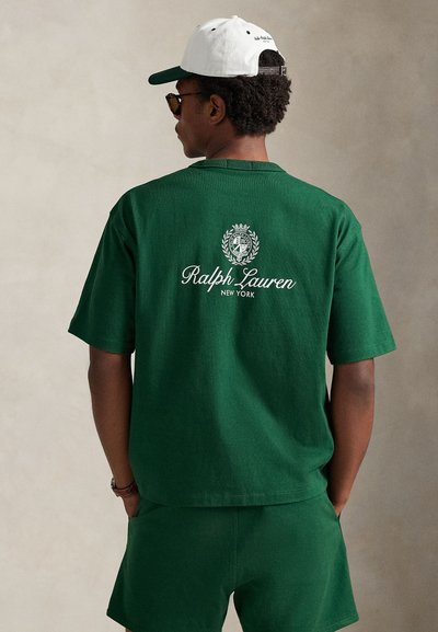 Σκούρο πράσινο βαμβακερό μπλουζάκι με κυκλικό λογότυπο και το κείμενο "Ralph Lauren New York" σε λευκό στην πίσω πλευρά. Το μοντέλο φοράει γυαλιά ηλίου και καπέλο.