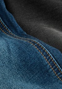 Teren de denim de un albastru închis, cu cusături portocalii, suprapus peste un textil moale de culoare neagră, evidențiind texturi și culori contrastante.