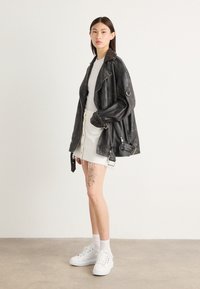 Schwarze Leder-Motorradjacke mit großem Kragen, kombiniert mit einem weißen Jeansrock mit fransigen Kanten und weißen Sneakers.