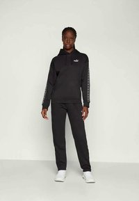 Set di felpa e pantaloni neri. La felpa ha una tasca frontale, berretto con lacci e logo; i pantaloni sono a gamba dritta con logo sulla gamba.