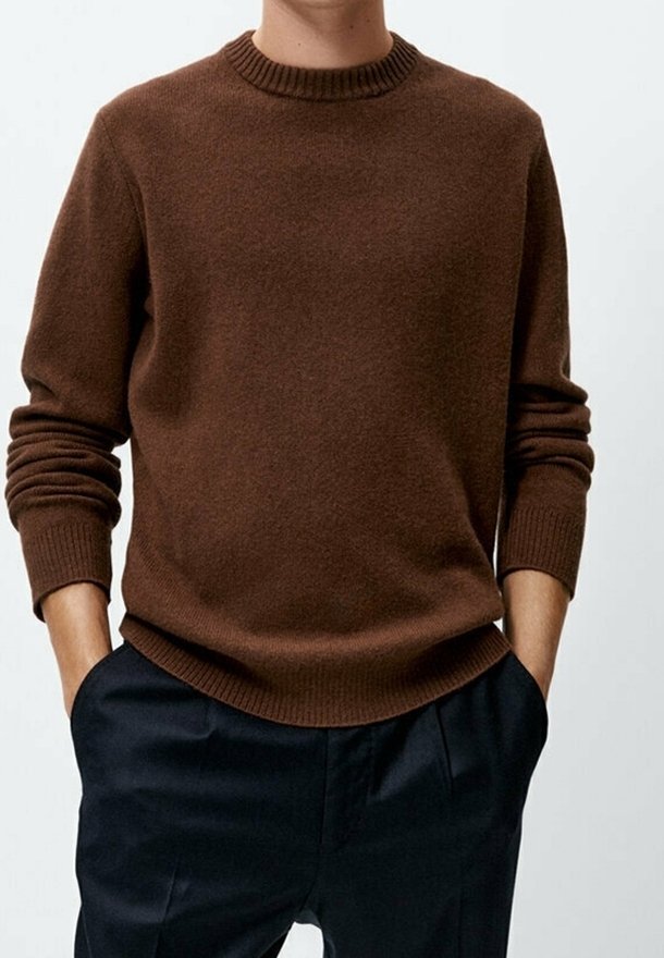 Brązowy sweter dziany z prążkowanym okrągłym dekoltem i długimi rękawami, zestawiony z ciemnymi spodniami, charakteryzującymi się luźnym krojem i gładką teksturą.