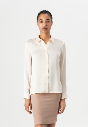 Cream long-sleeve blouse with button-down front, featuring a subtle textured pattern. Paired with a fitted beige ribbed skirt.