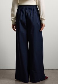 Pantalons larges bleu marine avec une taille élastique, fabriqués dans un tissu lisse. Présente une coupe soignée avec des poches latérales, associés à un pull écru.