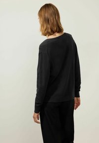 Svart stickad tröja med vid halsringning, sänkta axlar och ribbade muddkanter. Slät textur, något avslappnad passform, slutar vid höfterna.