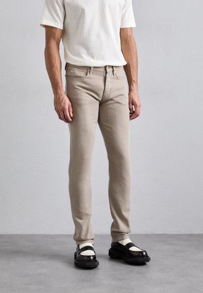 Beige bavlněné džíny s úzkým střihem, zdobené jemnými švy. Kombinované s černými platformovými botami a textura bílou košilí.