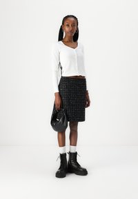 Haut court à manches longues blanc avec des boutons, jupe en tweed noir, bottes de combat noires et sac à main noir avec une poignée nouée.