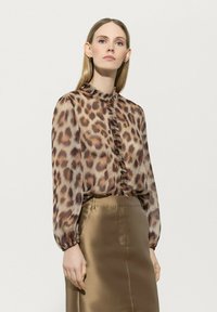 Bluse mit Leopardenmuster und Rüschenausschnitt sowie Rüschenfront, lange Ärmel. Kombiniert mit einem glatten, satinierten, hellbraunen Rock.
