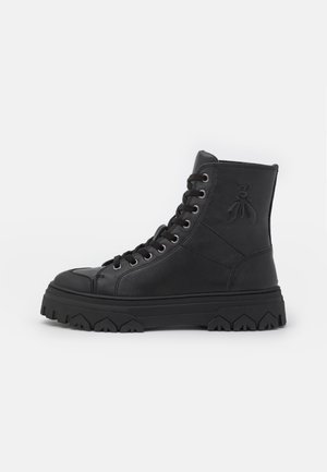 Botte montante en cuir noir avec semelle épaisse et robuste, fermeture à lacets à l'avant, et détail embossé d'insecte sur le côté de la cheville.