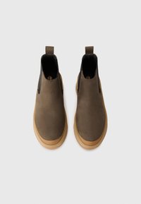 Brune lær Chelsea støvler med en sort elastisk sidepanel og en tan gummisål. Har en løftestrop bagpå for let påtagning.