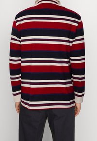 Camisa polo de manga larga con rayas horizontales en rojo, azul marino y crema; tela texturada con un acabado suave; cuello estándar.