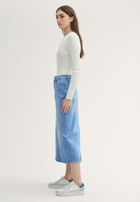 Long-sleeve, ribbed white top, paired with a high-waisted, light blue denim midi skirt and white sneakers with gray accents.
