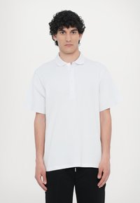Hvit polo-skjorte med klassisk krage, korte ermer og placket med tre knapper. Glatt stoff, avslappet passform og ingen synlige mønstre.