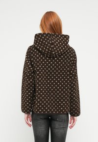 Kurtka z polaru z kapturem, o brązowej bazie z kontrastującym kremowym wzorem w kropki, długimi rękawami i miękkim, teksturowanym wykończeniem.