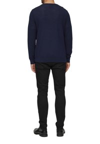 Marineblauwe trui van zachte stof, met lange mouwen, een ronde hals en een aansluitend ontwerp. Gecombineerd met zwarte broeken en schoenen.