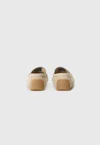 Beige suede loafers with a low heel, featuring a branded back and stitching details. Smooth texture and slip-on design.