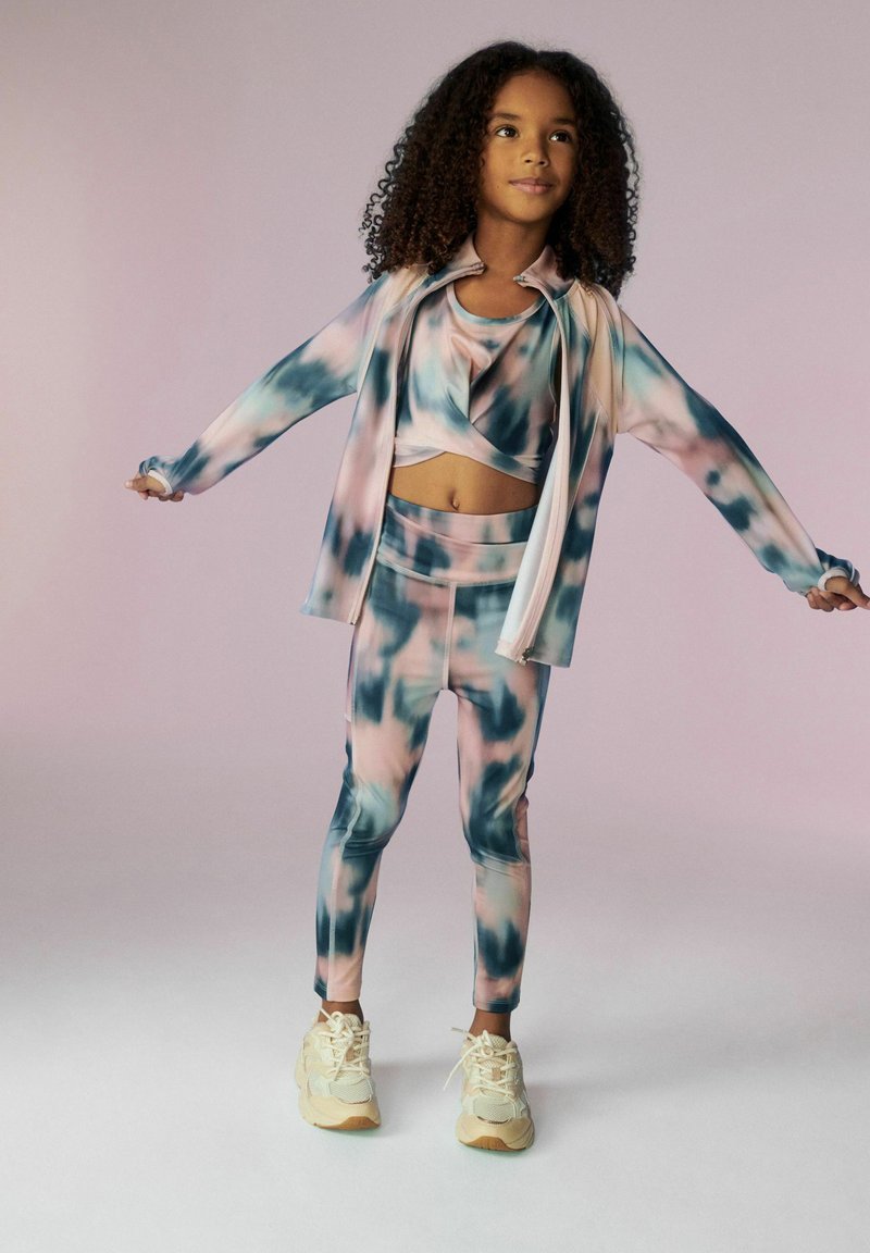 Souprava sportovního oblečení s růžovým, modrým a bílým tie-dye vzorem. Obsahuje crop top, dlouhou bundu a přiléhavé legíny. Texturovaná látka.