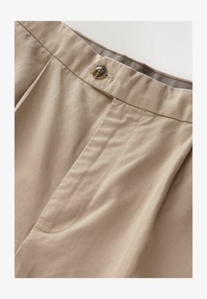 Beige bukser med en glat overflade, en enkelt knaplukning og frontfold. Inkluderer sidelommer og en syet talje.