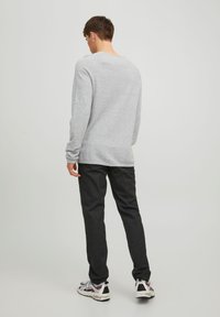 Felpa grigia a maniche lunghe, dal morbido tessuto, con collo rotondo, abbinata a pantaloni scuri e sneakers bianche con accenti argento.