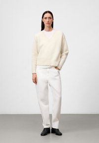 Ivore gebreide trui met een V-hals en geribbelde zoom, gecombineerd met witte wijde broek. De outfit wordt aangevuld met zwarte enkelboots.