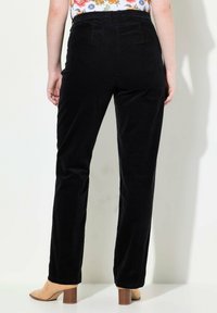 Pantaloni in corduroy neri con un design a gamba dritta, caratterizzati da una vita alta e tasche posteriori visibili; abbinati a scarpe con tacco blocco color cammello.
