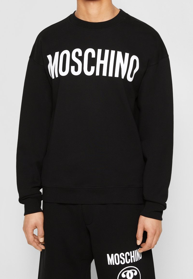 Černá mikina z měkké látky s velkým bílým logem "MOSCHINO" na přední straně. Klasický kulatý výstřih a uvolněný střih.