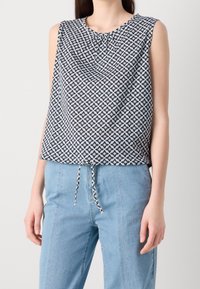 Top bez rukávů s kulatým výstřihem, zdobený geometrickým hvězdným vzorem v námořnické modři a bílé. Šňůrkový detail na spodním lemu.