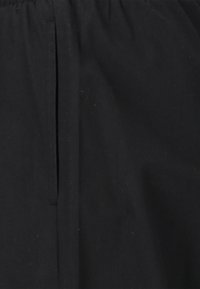 Svart plagg med en slät textur, som har en vertikal slits och elastisk midja. Tyget verkar lätt och har minimala rynkor.