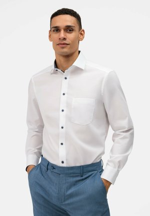 White button-up shirt with a pocket, featuring blue buttons. Worn with blue textured trousers. Smooth fabric, slim fit design.