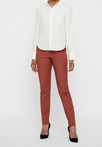 White long-sleeve shirt with button closure paired with rust-colored fitted pants and black high-heeled shoes. Simple, tailored design.