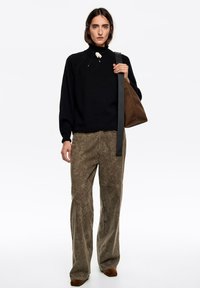 Czarny dziany sweter z wysokim kołnierzem, zestawiony z oliwkowozielonymi spodniami o szerokich nogawkach i teksturowanym wzorze. Brązowa torba z paskiem.