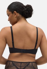 Sujeción negra con tirantes ajustables, cierre de gancho y ojal en la parte posterior, y textura de tela suave. Diseñada para comodidad y soporte.