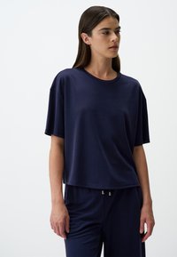 T-shirt a maniche corte blu navy con scollatura rotonda, vestibilità comoda e texture liscia. Abbinato a pantaloni coordinati con dettagli dorati.