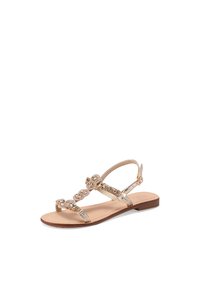 Sandal flat con una soletta in pelle color cammello, cinturini metallici oro, dettagli intrecciati decorativi e chiusura con fibbia alla caviglia.