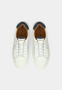 Λευκά δερμάτινα sneakers με τρύπες στη μύτη, γκρί αντίθεση στη φτέρνα, καφέ εσωτερική επένδυση και λευκά κορδόνια. Το όνομα μοντέλου "REPLAY" είναι τυπωμένο.