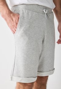 Pantalones cortos de algodón gris claro con cintura ajustable, bolsillos laterales y dobladillos enrollados que muestran una tela suave y texturizada.
