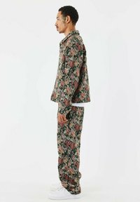 Conjunto de chaqueta y pantalones de estampado floral en negro con rosas rosas y verdes, con un ajuste holgado y un diseño con cuello. Zapatillas blancas completan el look.