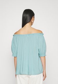 Blusa leve azul clara com ombros à mostra, mangas bufantes, decote franzido e punhos elásticos; tecido fluido e texturizado.