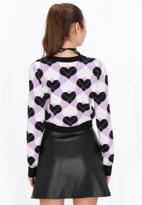Maglione a maglia viola con motivo a cuori bianco e nero, polsini a costine e vita nera, abbinato a una gonna in faux pelle nera.