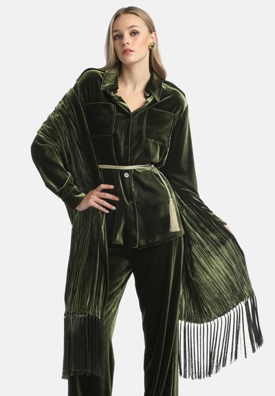 Completo in velluto verde caratterizzato da una camicia con bottoni, due tasche, maniche ampie e uno scialle con frange, completato da una cintura con nappine.