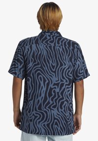Camicia a maniche corte di colore blu navy con un motivo a onde testurizzate in blu chiaro, dotata di colletto e orlo dritto.