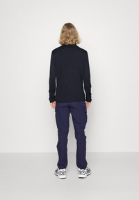 Camicia a maniche lunghe di colore blu navy con colletto rotondo, abbinata a pantaloni cargo di colore blu scuro e sneakers bianche con dettagli neri e grigi.
