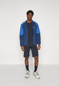 Lekka kurtka w kolorach niebieskim i granatowym z regulowanym kapturem, zestawiona z czarną koszulką, krótkimi spodniami i sportowymi butami.