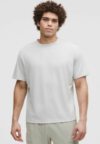 Camiseta de manga corta y cuello redondo en tejido gris claro con una textura suave y un corte relajado, combinada con pantalones de color claro.