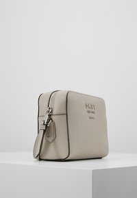 Borsa cosmetica in pelle beige con superficie strutturata, hardware in argento, chiusura con cerniera superiore e logo in rilievo sulla parte anteriore.