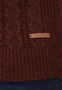 Garnkabelstickad tröja i mörk burgundy, med ribbad nederkant och ett lädermärke märkt "Pier One". Texturerad, ullblandad tyg.