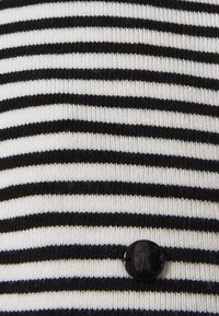 Schwarz-weißer, horizontal gestreifter Stoff mit einem kleinen, runden, schwarzen Knopf, der nahe der unteren rechten Ecke angenäht ist.