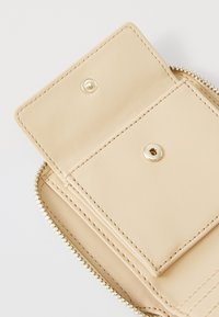 Beige Leder Geldbörse mit Reißverschluss, ausgestattet mit einer glatten Textur, einem Druckknopf-Fach und goldenen Hardware-Akzenten.