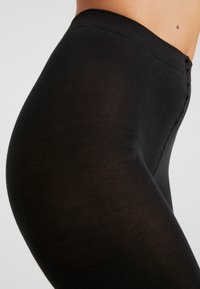 Schwarze Leggings mit einer glatten, elastischen Textur. Hoher Bund und seitliche Nähte sind sichtbar. Das Material wirkt weich und figurbetont.